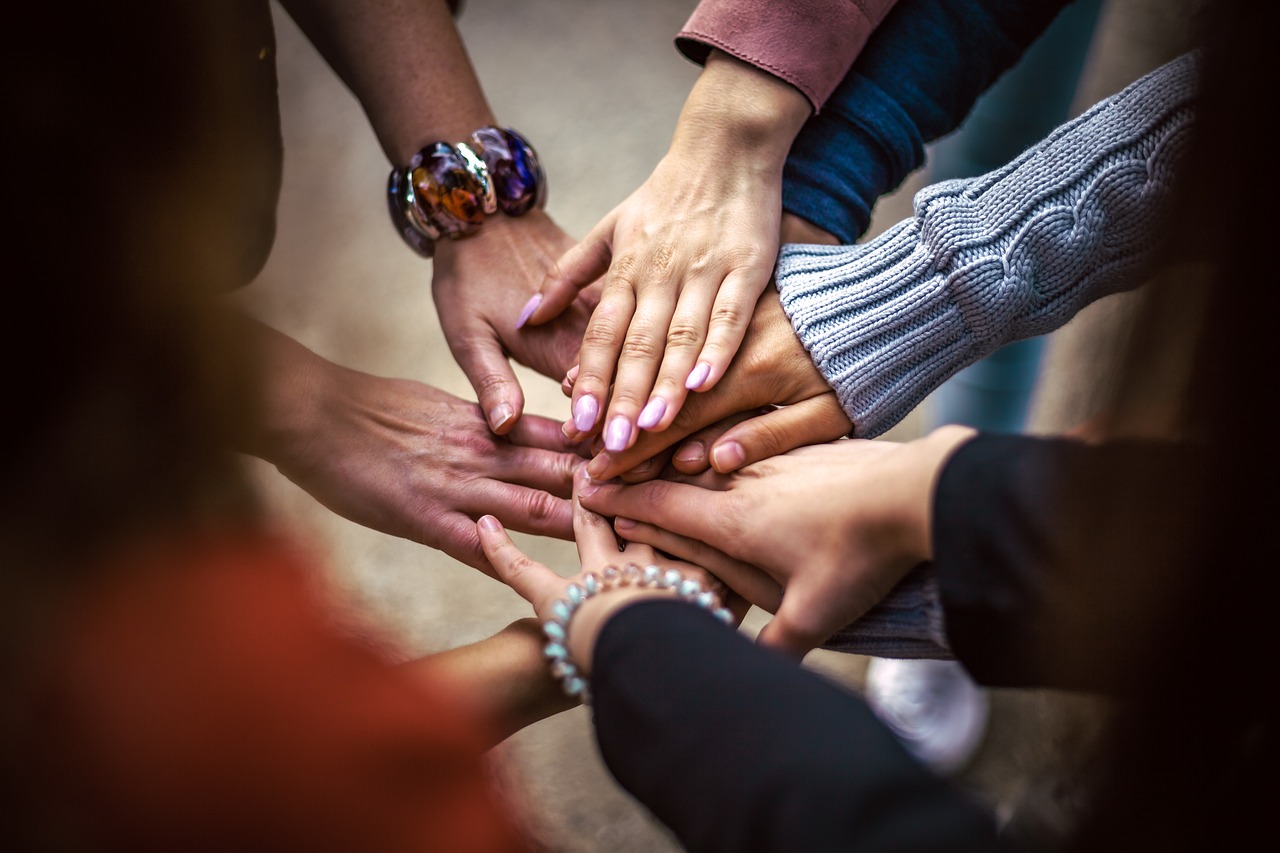 7 Leute die Hände zusammenschlagen und eine Gemeinschaft bilden